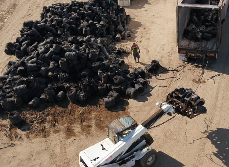 Large industrial vehicle lifting bundles of coiled drip tape into an open-back truck to be delivered to a Netafim recycling site.